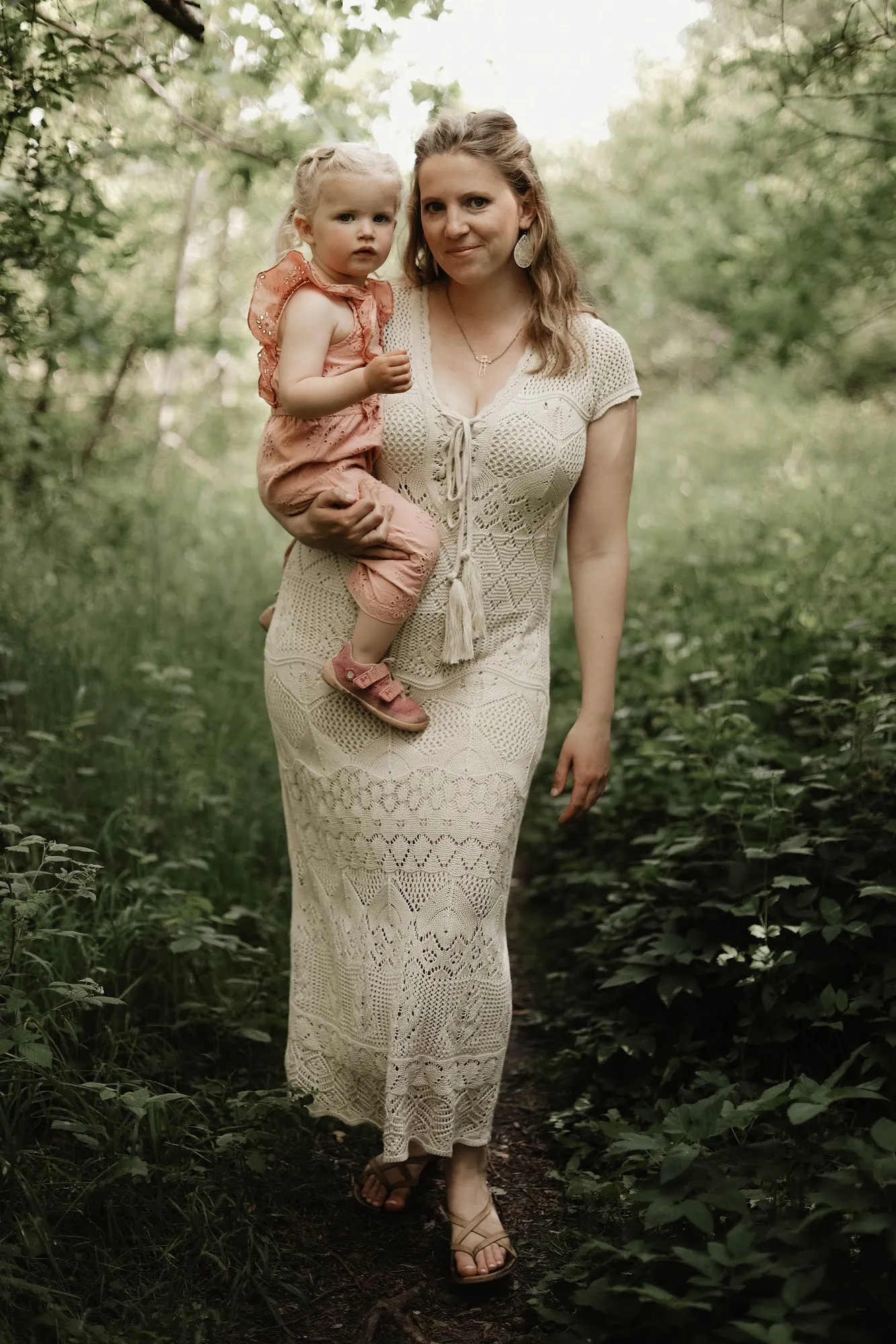 Mutter im hellen Kleid trägt ihre kleine Tochter im Grünen
